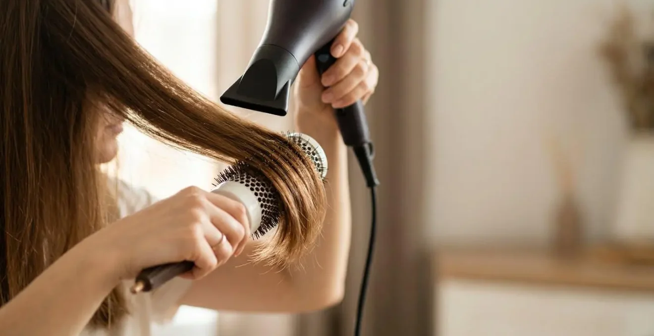 Mains féminines tenant une brosse ronde professionnelle et un sèche-cheveux sur cheveux brillants