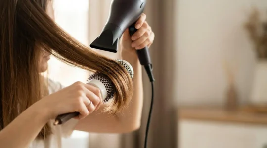Mains féminines tenant une brosse ronde professionnelle et un sèche-cheveux sur cheveux brillants