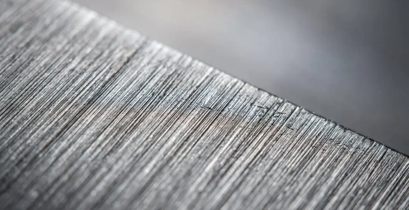Vue macro de la surface d'acier brossé montrant les micro-stries parallèles dirigeant la lumière de manière uniforme