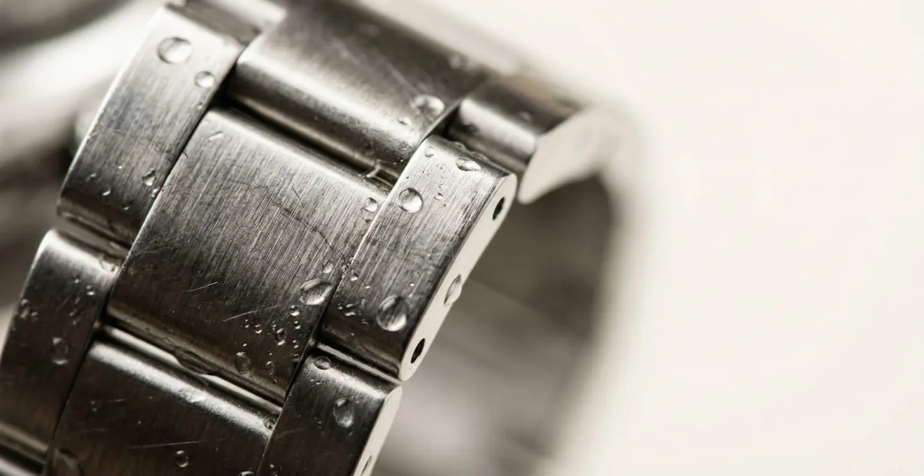 Gros plan macro d'un bracelet de montre en acier inoxydable avec eau et micro-gouttes, surface brossée détaillée sans texte visible