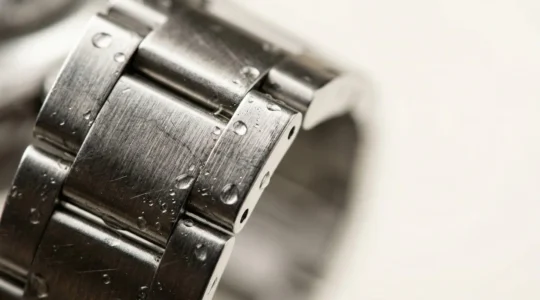 Gros plan macro d'un bracelet de montre en acier inoxydable avec eau et micro-gouttes, surface brossée détaillée sans texte visible